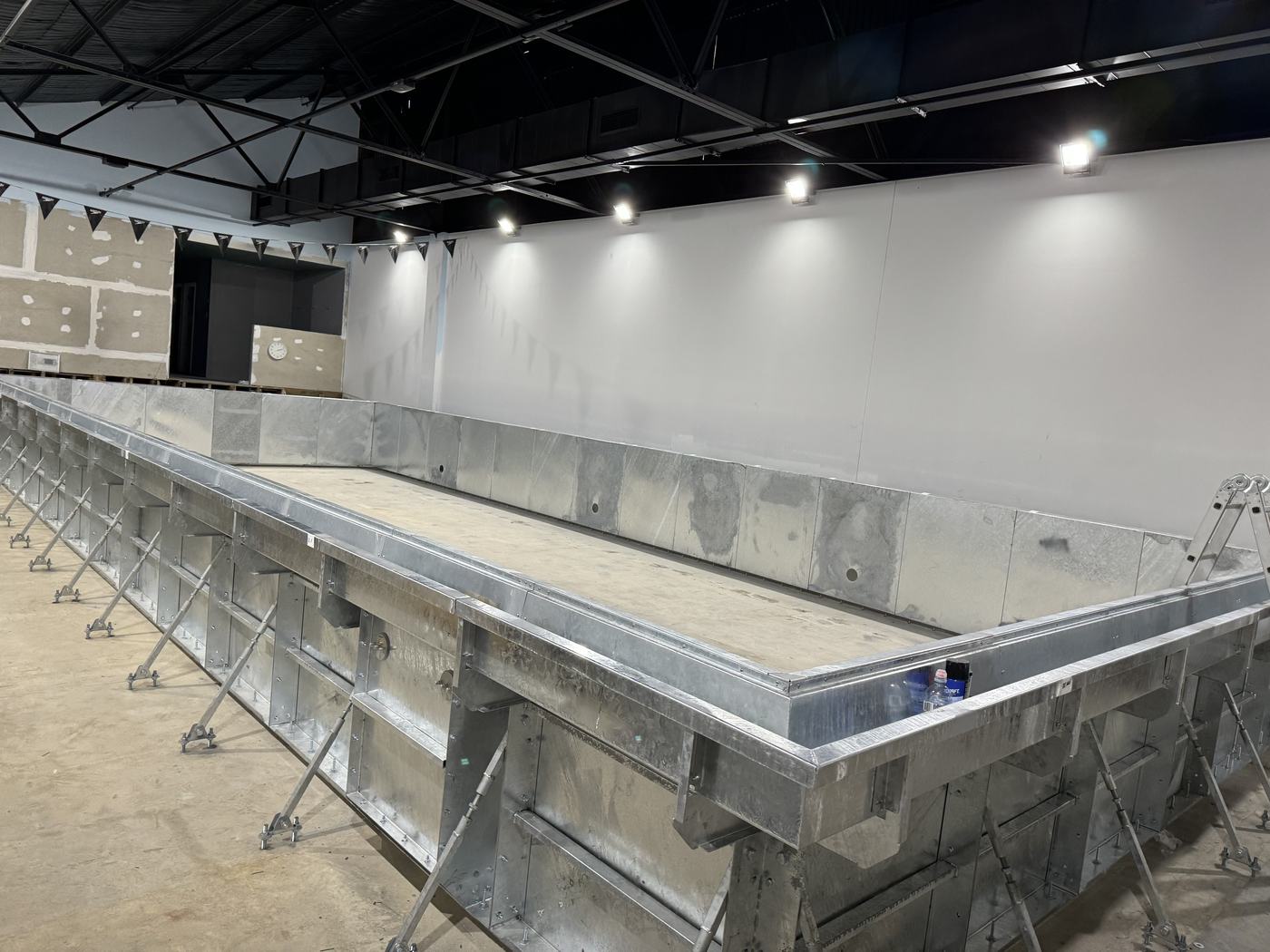Bare galvanised steel modular pool shell inside a building